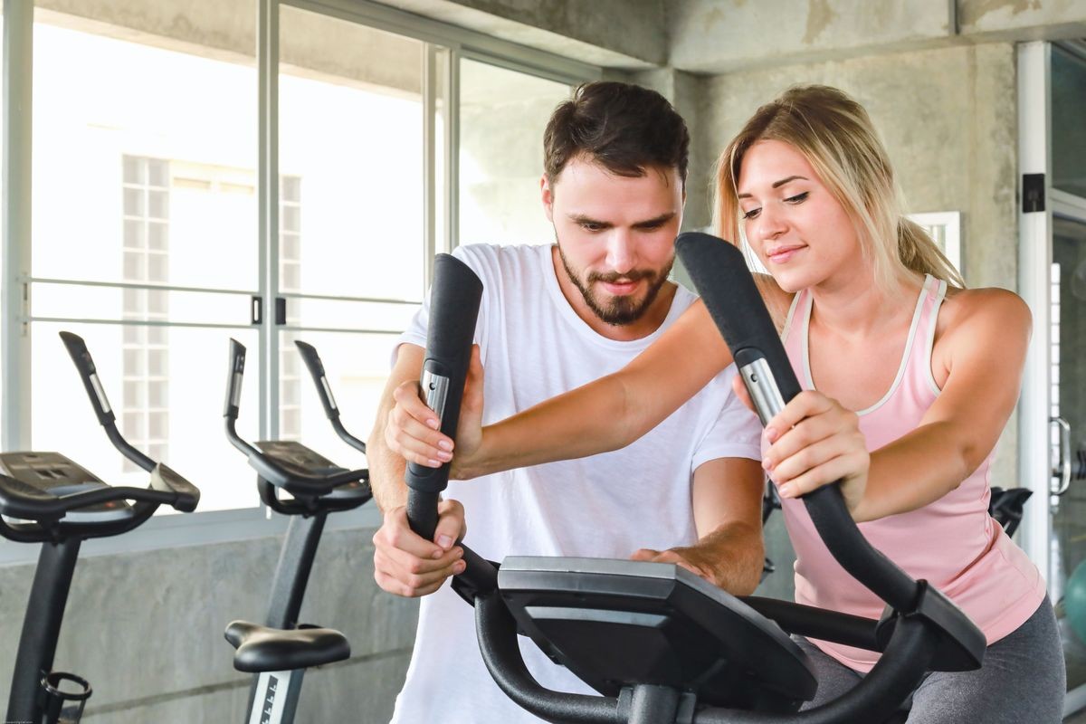 Handsome personal trainer with attractive young fitness girl coaching cardio training by bike in professional gym. Healthy, fitness,good health,fit and firm concept.